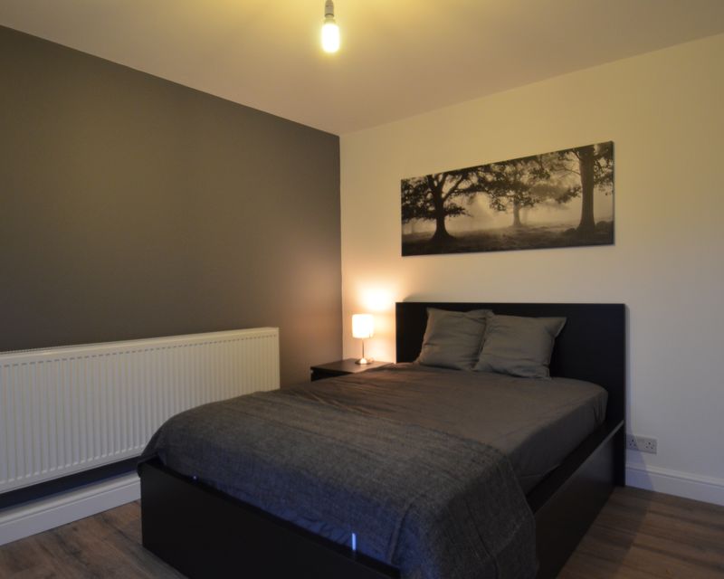 A double bedroom in one of our managed properties — grey feature wall, warm bedside lamp and framed woodland print.